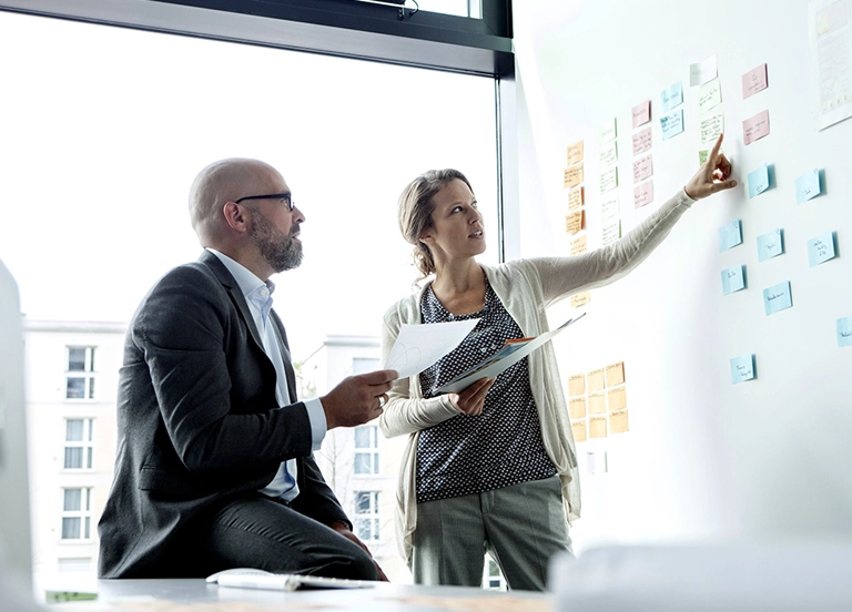 Two colleagues in a planning session and pointing to sticky notes