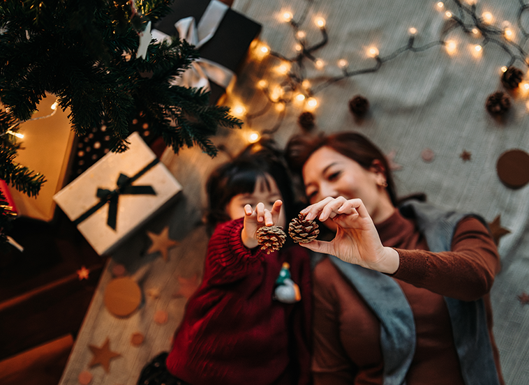 mon and child under Christmas tree with pine cones